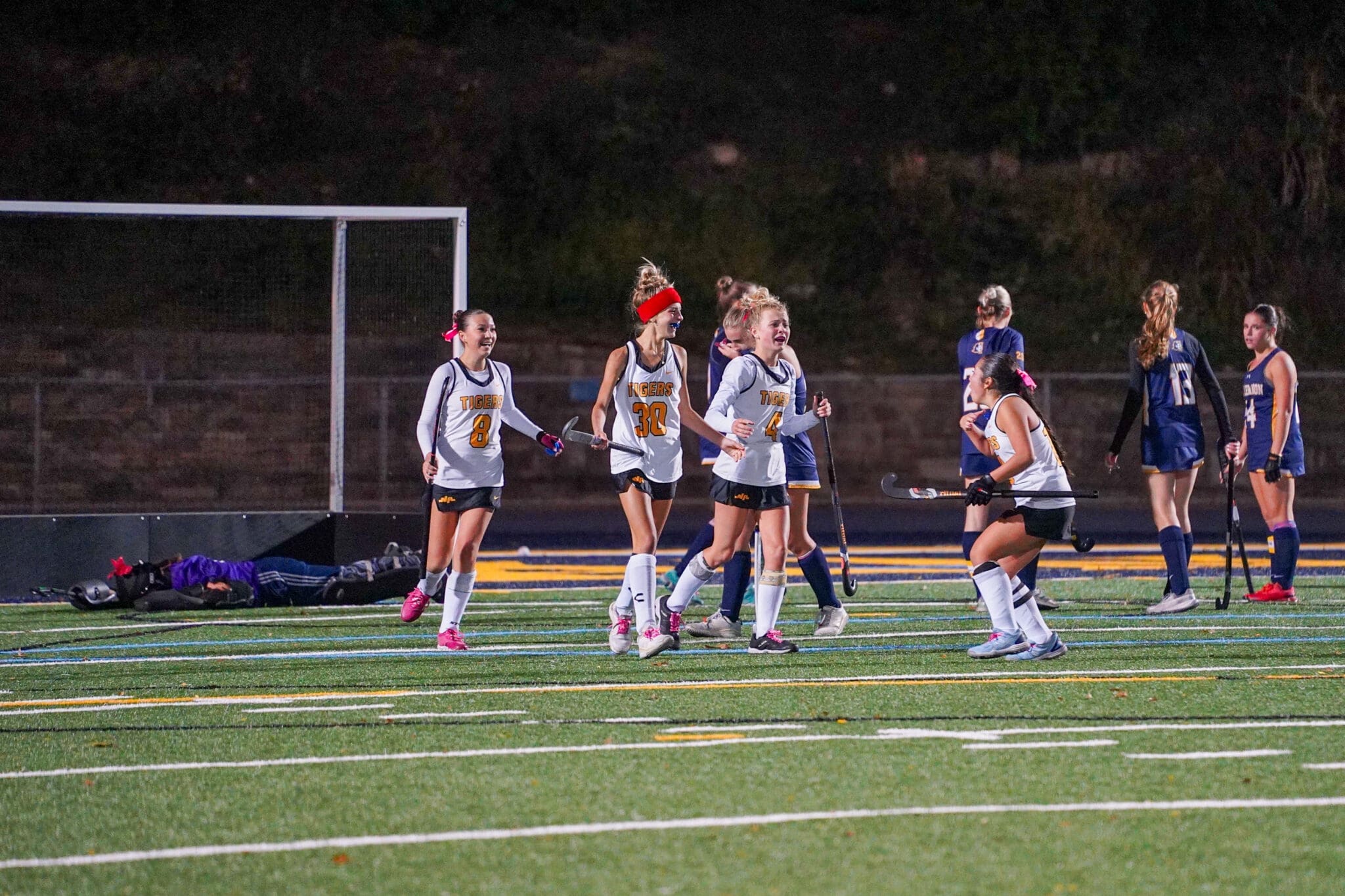 Field hockey players celebrate near the goalpost during a night match, showcasing team spirit and competition.