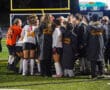 North Allegheny field hockey team huddles on the field, preparing for a match under stadium lights.