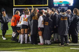 North Allegheny field hockey team huddles on the field, preparing for a match under stadium lights.