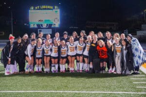 Group photo of a field hockey team smiling on a stadium field at night.