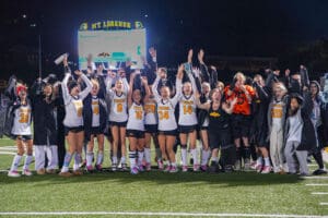 Victorious sports team celebrating on the field at night with scoreboard in the background.