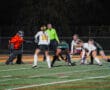 Girls' field hockey match at night with players competing for the ball near the goal.