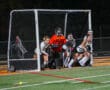 Goalie and field hockey team defending the goal during a night game on artificial turf.