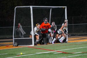 Goalie and field hockey team defending the goal during a night game on artificial turf.