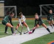 Field hockey players compete for ball during a night match on artificial turf.