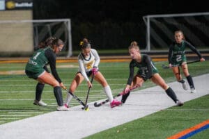 Field hockey players compete for ball during a night match on artificial turf.