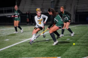 Girls' field hockey match at night, players in action on the field competing for control of the ball.