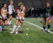 Field hockey players in action under stadium lights, two teams competing, focus on player with ball.