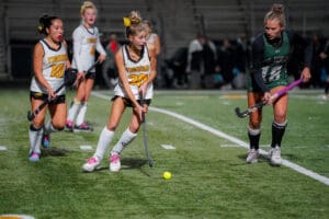 Field hockey players in action under stadium lights, two teams competing, focus on player with ball.