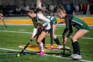 Field hockey players in action during a night match on a brightly-lit field.