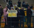 Fans holding a Let's Go Alexis #11 sign in a stadium cheering section at a night sports event.