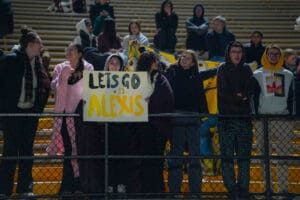Fans holding a Let's Go Alexis #11 sign in a stadium cheering section at a night sports event.