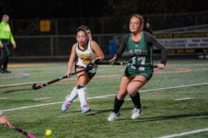 Field hockey players in action during a lively game on a lit field at night.