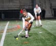 Female field hockey player dribbles ball under stadium lights during a night match.