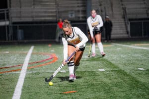 Female field hockey player dribbles ball under stadium lights during a night match.