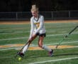 Field hockey player in action, dribbling the ball on a green turf field during a night match.