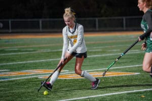 Field hockey player in action, dribbling the ball on a green turf field during a night match.