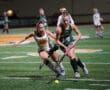 Two field hockey players compete intensely for the ball on a green turf field.