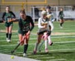 High school field hockey game, players in action on turf, focus on two athletes competing for the ball.