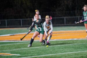 Field hockey players competing for the ball on a sports field during a night match.