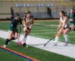 Field hockey players in action, competing for the ball on a green turf field, intense athletic moment.