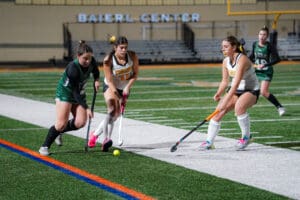 Field hockey players in action, competing for the ball on a green turf field, intense athletic moment.