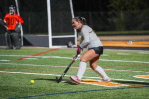 Field hockey player poised to hit the ball towards the goal on a brightly lit turf field.