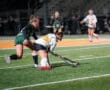 Two field hockey players competing under stadium lights on a turf field.