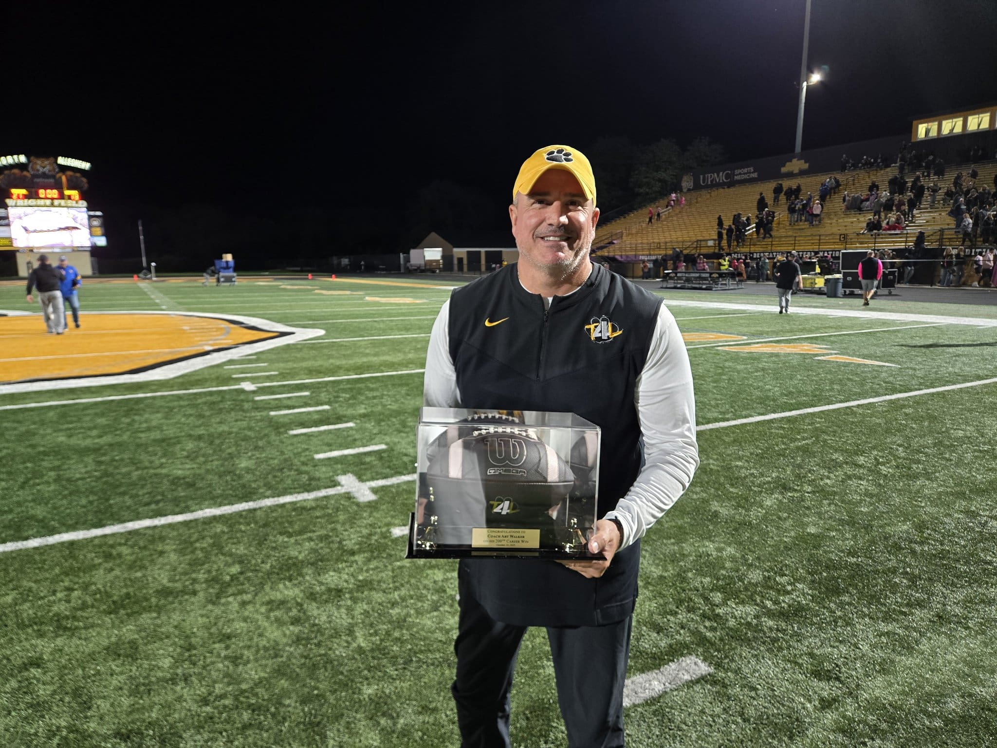 Man holding football trophy on field after night game, smiling.