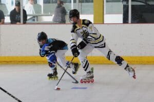 Two players competing in roller hockey match, wearing helmets and gear, on an indoor rink.