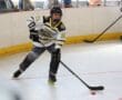 Roller hockey player in action, aiming at puck during an indoor match with fans watching from the sidelines.