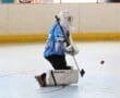 Hockey goalie in blue jersey defends the net during an indoor roller hockey game.