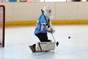 Hockey goalie in blue jersey defends the net during an indoor roller hockey game.