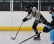 Roller hockey player in black and white uniform taking a shot, with a defender nearby on the rink.