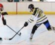 Two roller hockey players in action on an indoor rink, one attempting a shot.