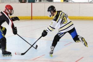 Two roller hockey players in action on an indoor rink, one attempting a shot.