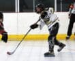 Roller hockey player in action, wearing black and white gear, preparing to strike the puck on an indoor rink.