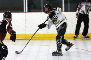 Roller hockey player in action, wearing black and white gear, preparing to strike the puck on an indoor rink.