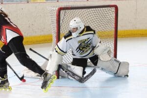 Roller hockey goalie makes a save against an attacking player in a match.
