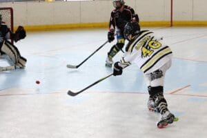 Inline hockey player taking a shot on goal while the goalie prepares to block. Action-packed game moment.