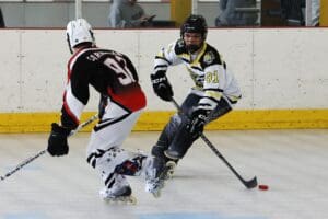 Two inline hockey players competing on the rink, one in white and yellow, the other in black and red jerseys.