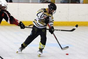 Roller hockey player in action, wearing striped jersey, about to hit puck while opponent defends.