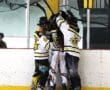 Hockey players in striped uniforms celebrate a goal near the ice rink boards.