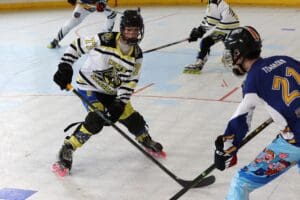 Youth roller hockey match with players in action, wearing vibrant jerseys and helmets, on an indoor rink.