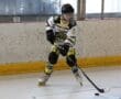 Roller hockey player in action, wearing yellow and black jersey, handling puck on rink.