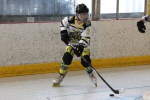 Roller hockey player in action, wearing yellow and black jersey, handling puck on rink.