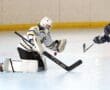 Roller hockey goalie in action making a crucial save during a match on an indoor rink.