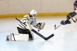 Roller hockey goalie in action making a crucial save during a match on an indoor rink.