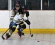 Hockey players in intense action during a competitive match with sticks and puck on a roller rink.