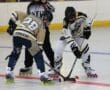 Two inline hockey players face off, competing for the puck on the rink with a referee observing.